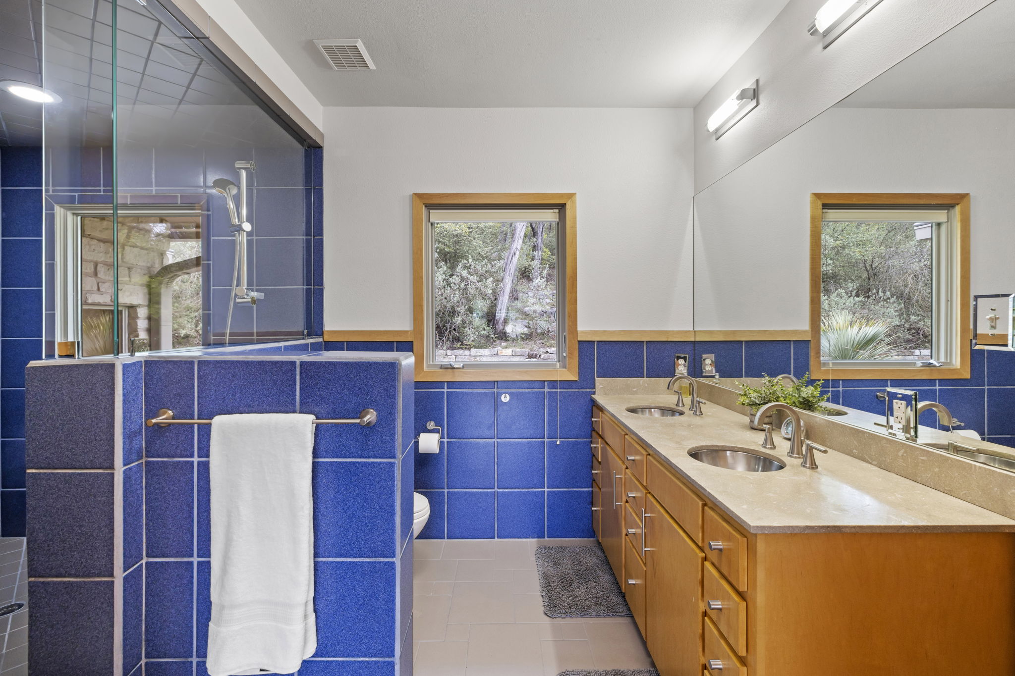701 Yaupon Valley Road West Lake Hills, TX 78746 - Photo 18 of 40 In the primary bathroom, cool blue tile, a large walk-in shower, dual vanities, and multiple windows create a bright and refreshing space.