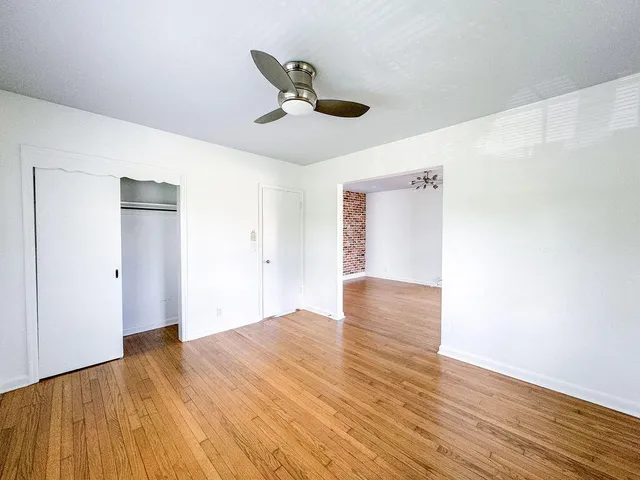 a view of an empty room with wooden floor and a ceiling fan