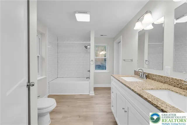 a bathroom with a granite countertop sink toilet mirror and bathtub