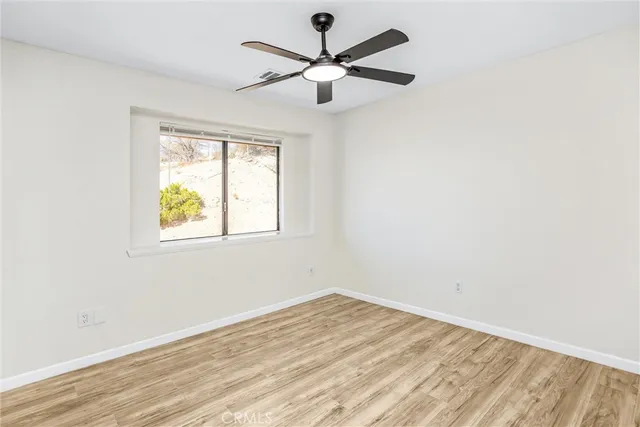 an empty room with wooden floor ceiling fan and windows