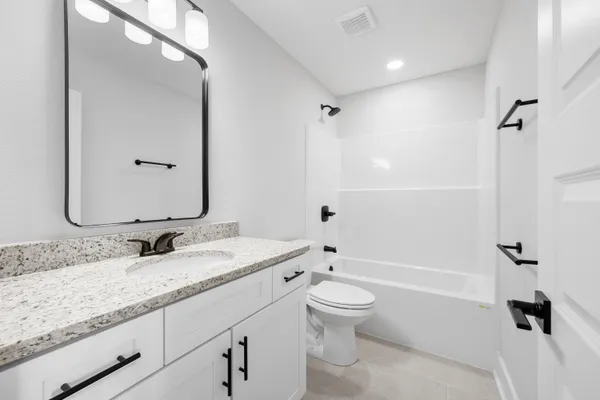 a bathroom with a granite countertop bathtub shower sink mirror vanity and toilet