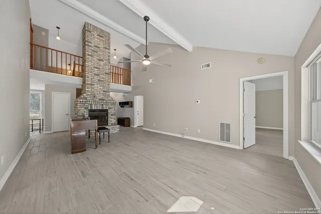 an empty room with wooden floor fireplace and windows