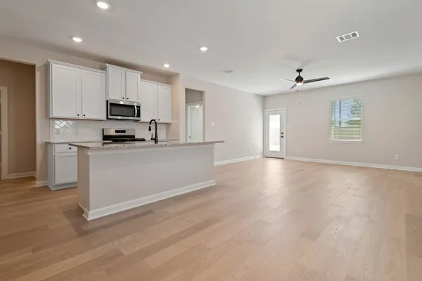 a kitchen with stainless steel appliances a microwave a stove a sink dishwasher a refrigerator and white cabinets with wooden floor