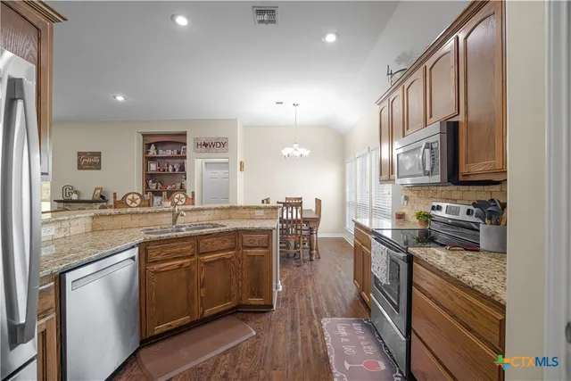 a kitchen with stainless steel appliances granite countertop a stove top oven a sink dishwasher a dining table and chairs with wooden floor