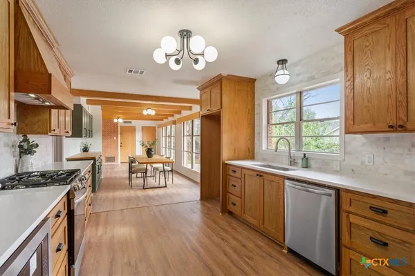 a open kitchen with stainless steel appliances granite countertop a stove top oven a sink dishwasher a dining table and chairs with wooden floor