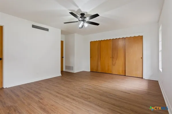a view of an empty room with wooden floor and a ceiling fan