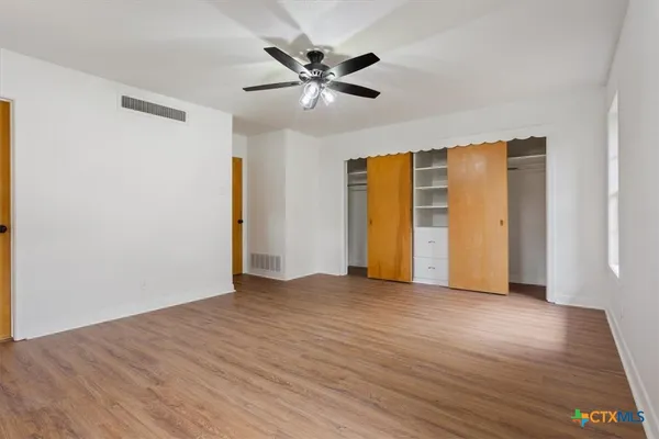 a view of an empty room with wooden floor and a ceiling fan