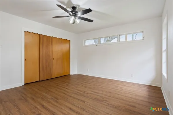 a view of an empty room with wooden floor and a ceiling fan