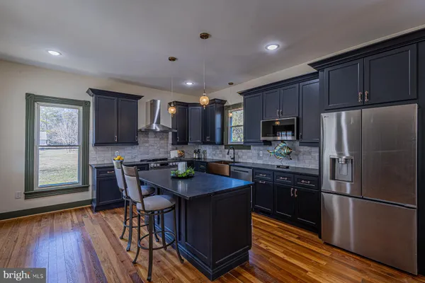 a kitchen with stainless steel appliances granite countertop wooden floors a stove a microwave a center island and a refrigerator