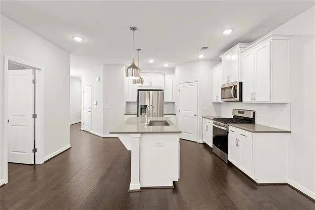 a kitchen with stainless steel appliances kitchen island granite countertop a stove a sink a refrigerator and white cabinets with wooden floor