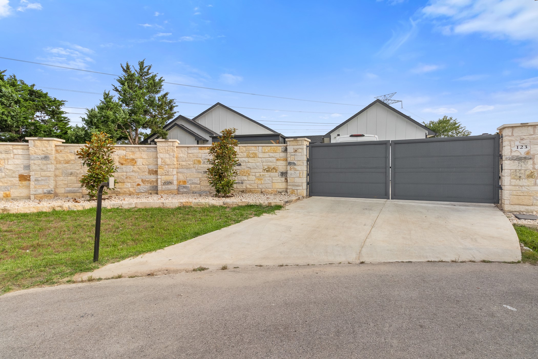 123 Zacate Street Elgin, TX 78621 - Photo 26 of 33 Gated driveway entry featuring a stone-clad perimeter wall, dual dark gray gates, and mature landscaping