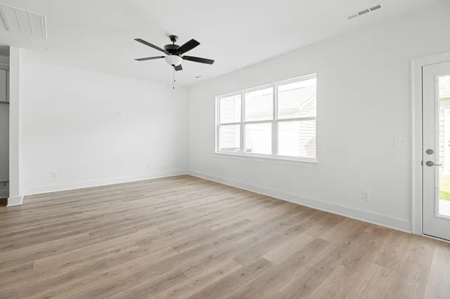 an empty room with wooden floor fan and windows