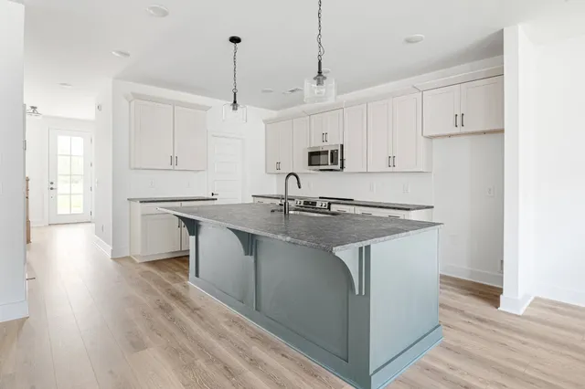 a kitchen with stainless steel appliances granite countertop a sink a stove a refrigerator and white cabinets with wooden floor