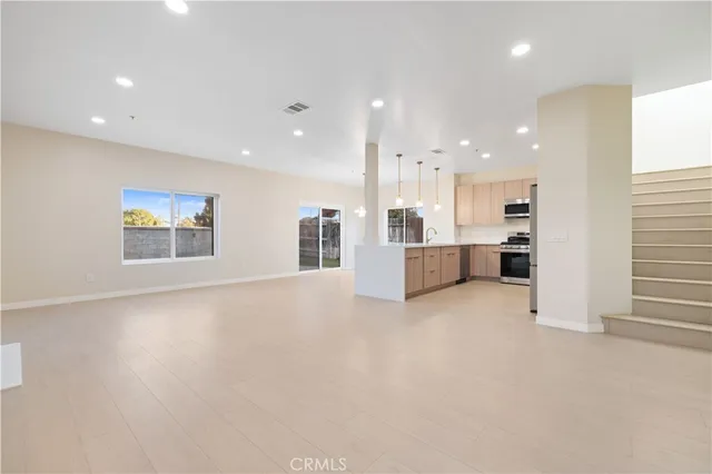 a view of an empty room with kitchen and window