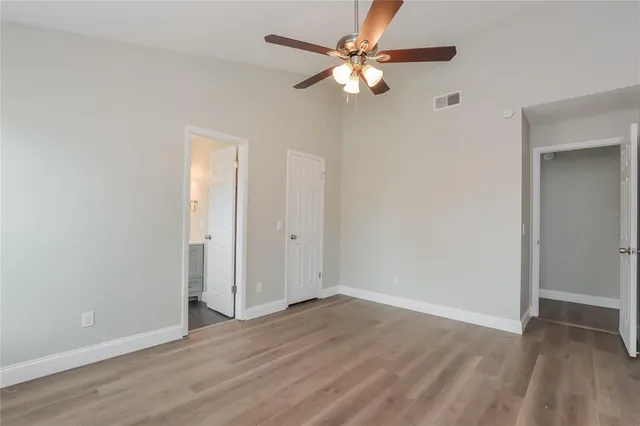 an empty room with wooden floor fan and windows