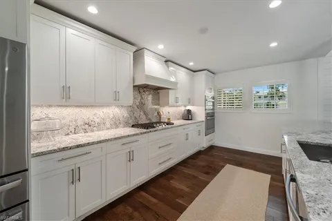 a large white kitchen with granite countertop white cabinets and stainless steel appliances