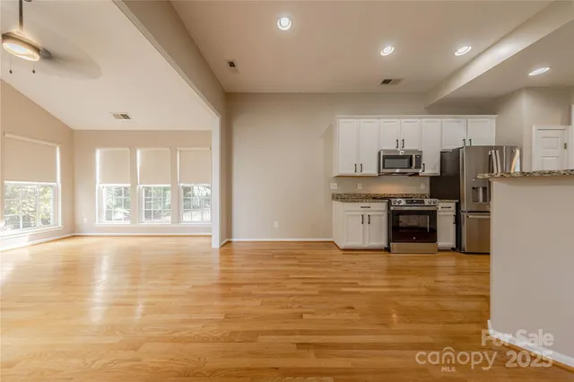 a large kitchen with granite countertop a stove a sink dishwasher a refrigerator and white cabinets with wooden floor