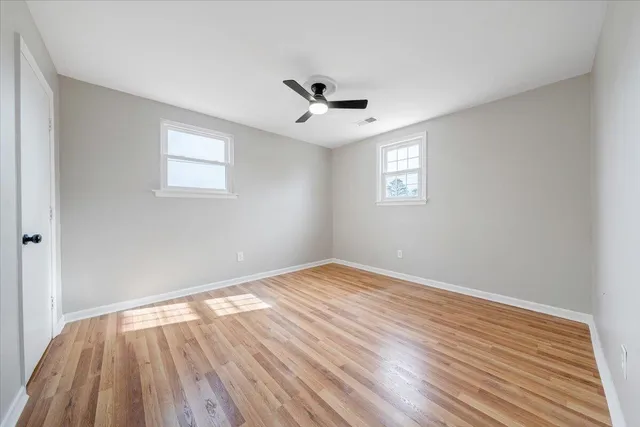 an empty room with wooden floor ceiling fan and windows