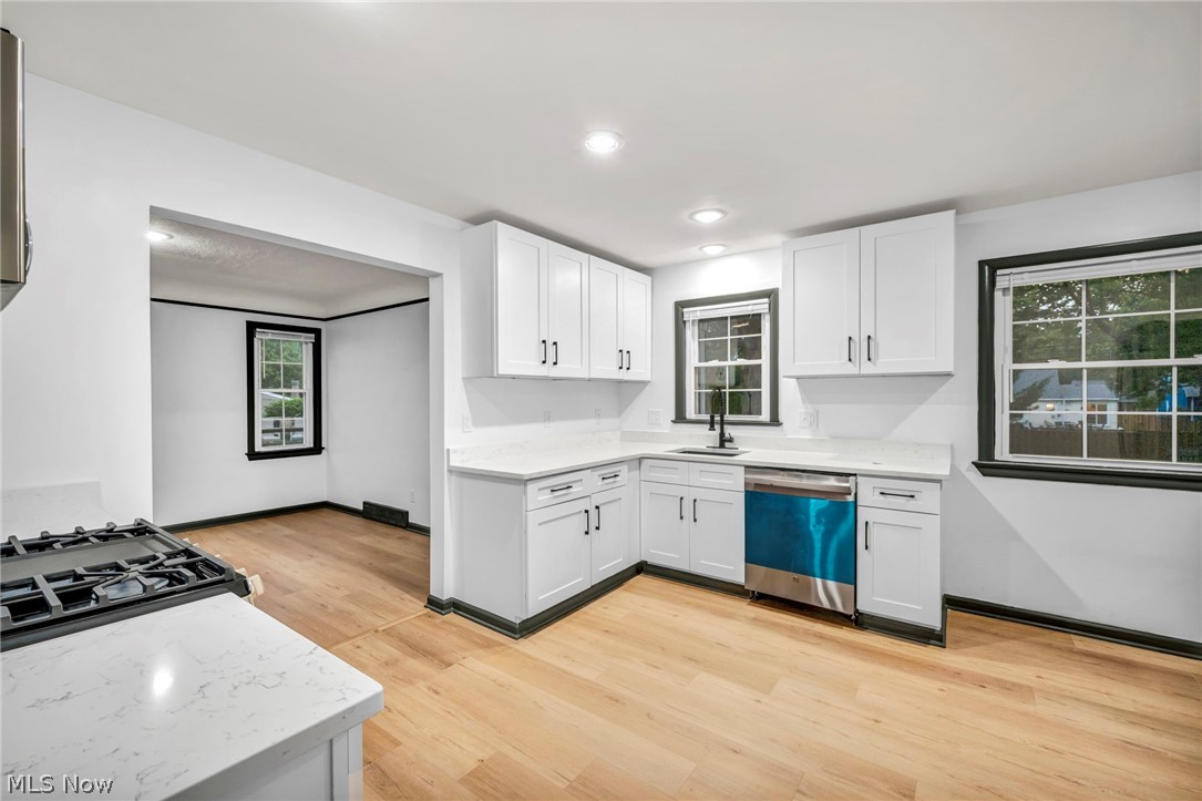 Kitchen featuring light stone countertops, stainless steel dishwasher, light wood-type flooring, sink, and white cabinetry