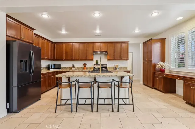 a kitchen with stainless steel appliances kitchen island granite countertop a refrigerator a stove a sink and a dining table with wooden cabinets