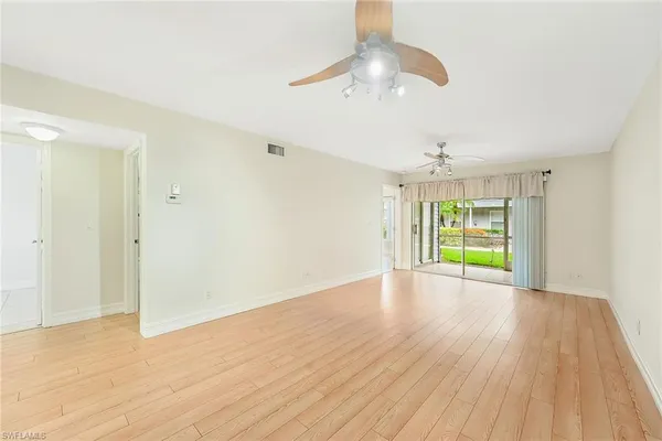 a view of an empty room with wooden floor ceiling fan