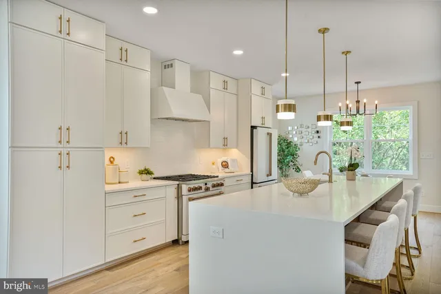 a kitchen with kitchen island a stove a refrigerator a sink dishwasher and white cabinets with wooden floor