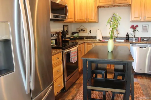 a kitchen with stainless steel appliances granite countertop a refrigerator a stove and a sink with wooden floor