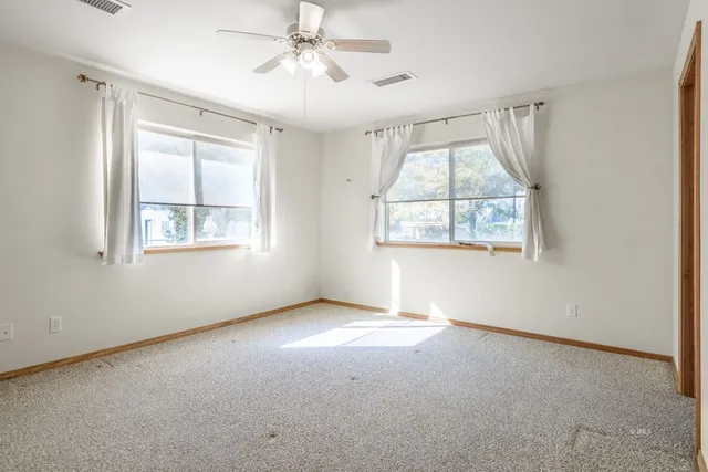 an empty room with windows and a chandelier fan