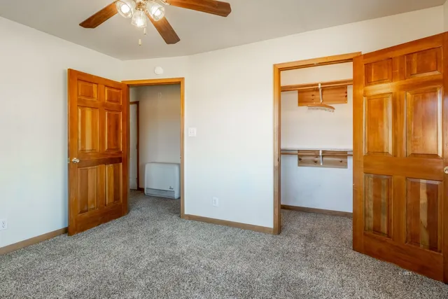 an empty room with chandelier fan and kitchen view