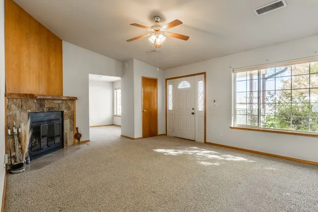 a view of a livingroom with a fireplace a ceiling fan and windows