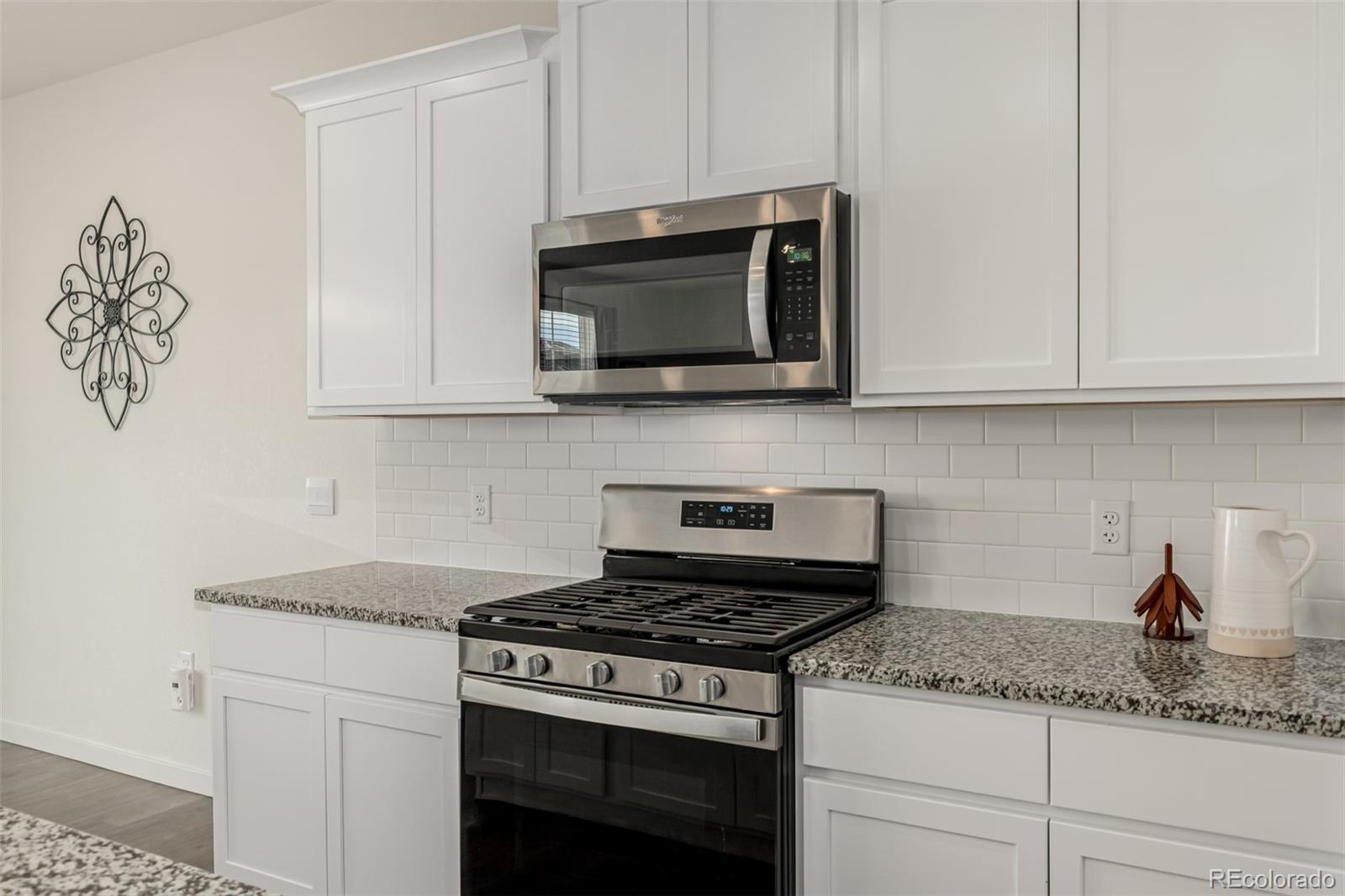 773 Allium Street Watkins, CO 80137 - Photo 7 of 46 a kitchen with granite countertop white cabinets and a stove top oven