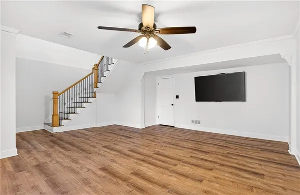 a view of an empty room with wooden floor and a ceiling fan