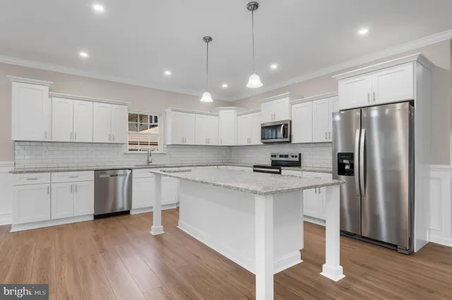 a kitchen with stainless steel appliances granite countertop a refrigerator a sink dishwasher a stove and white cabinets with wooden floor