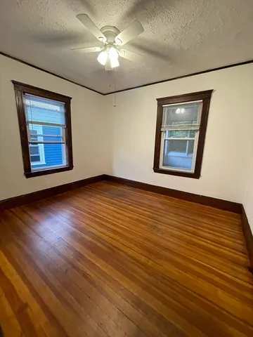a view of an empty room with wooden floor and a ceiling fan