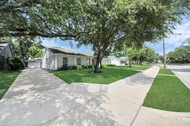 a view of a white house next to a yard with big trees
