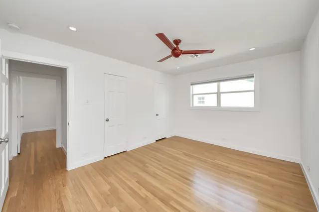 an empty room with wooden floor chandelier fan and windows