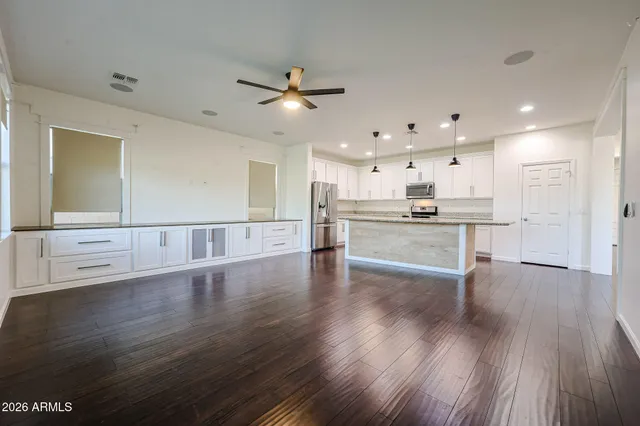 a view of an empty room with wooden floor and a kitchen