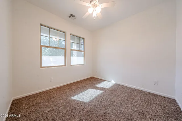 an empty room with a chandelier fan and windows