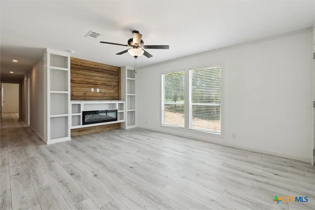 an empty room with wooden floor ceiling fan and windows