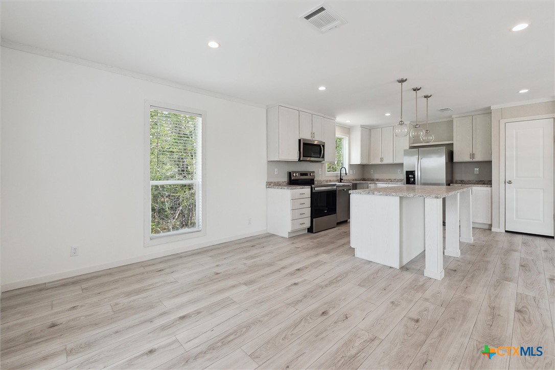855 Roosevelt Road Luling, TX 78648 - Photo 10 of 47 a kitchen with stainless steel appliances a microwave a stove a sink dishwasher and a refrigerator with wooden floor