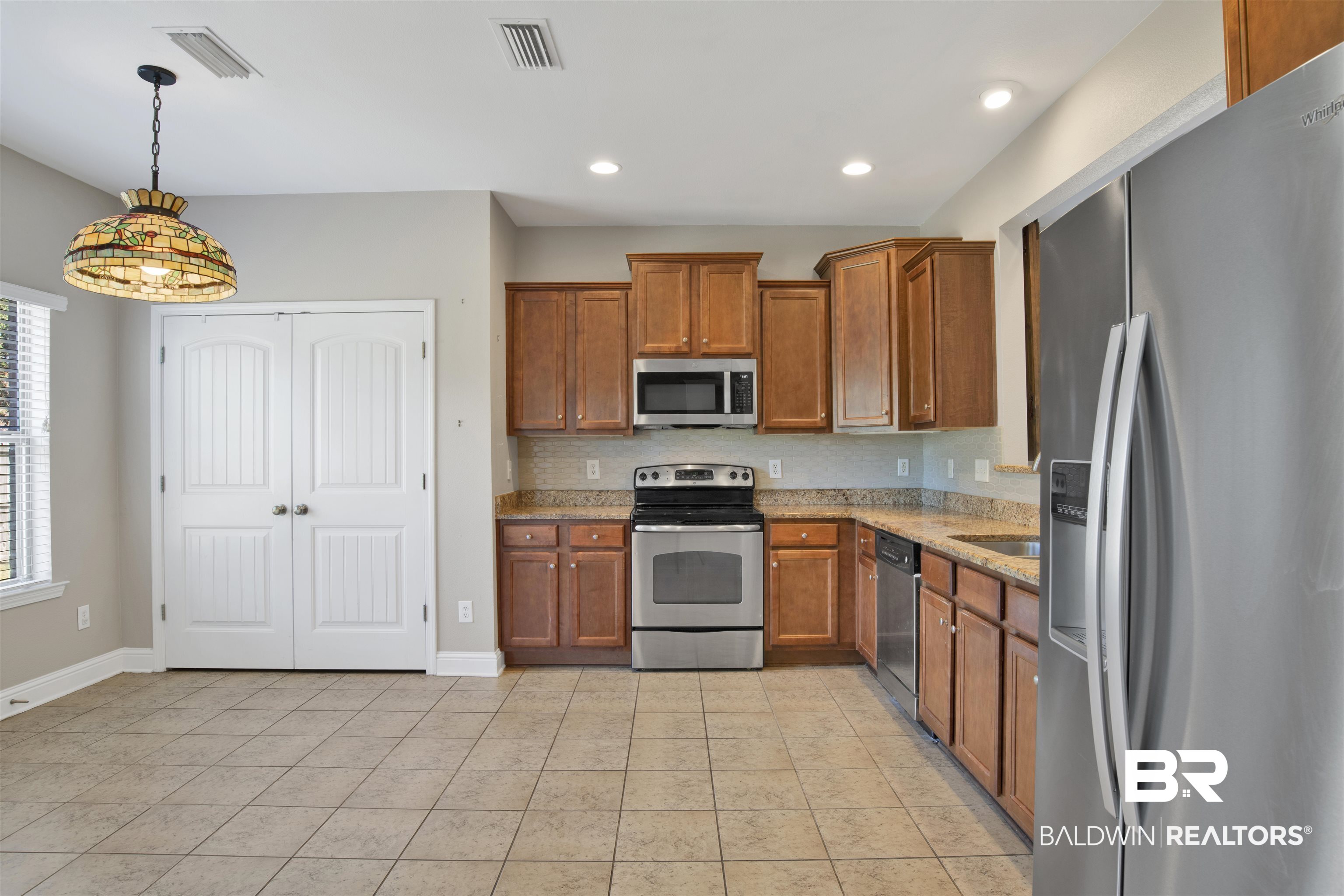 24159 Tullamore Drive Daphne, AL 36526 - Photo 12 of 31 Kitchen featuring tasteful backsplash, appliances with stainless steel finishes, hanging light fixtures, light stone counters, and light tile patterned floors