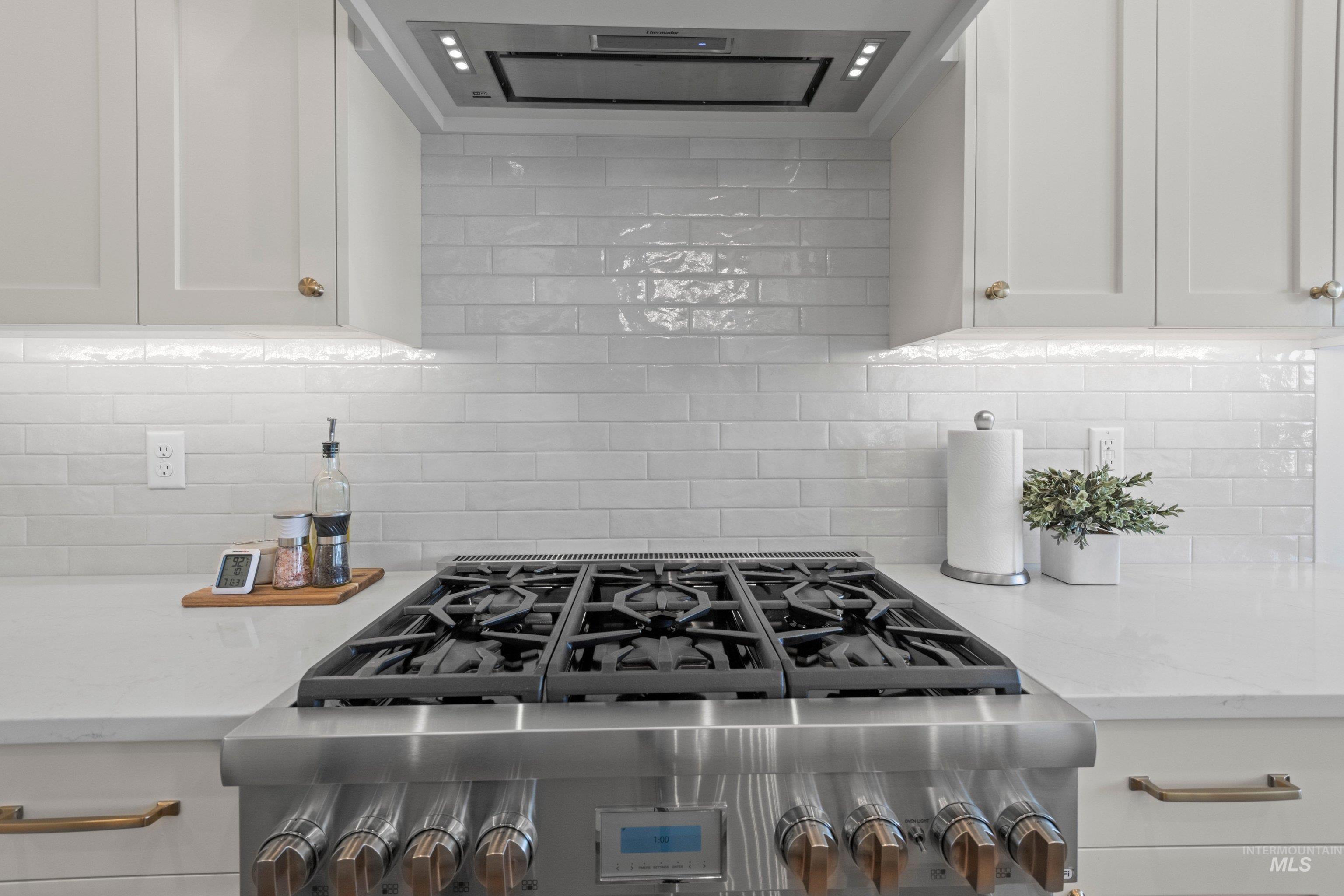 24990 Belgian Way Middleton, ID 83644 - Photo 15 of 50 Stainless steel professional range with a matching range hood, white subway tile backsplash, white shaker cabinetry, and light-toned countertops