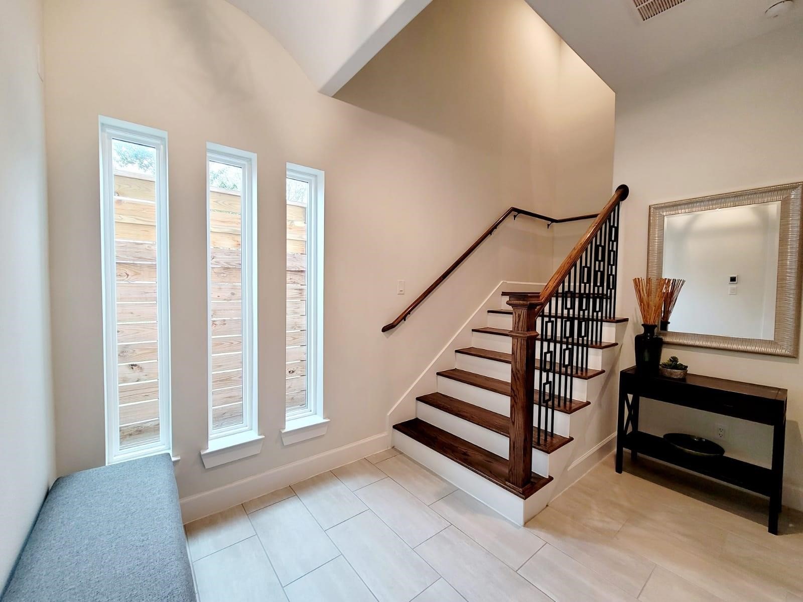 710 Delano Street, Unit A Houston, TX 77003 - Photo 14 of 32 Bright entryway with modern staircase featuring wooden steps and stylish railing. The space includes tall, narrow windows for natural light. Neutral tile flooring complements the clean, contemporary design.