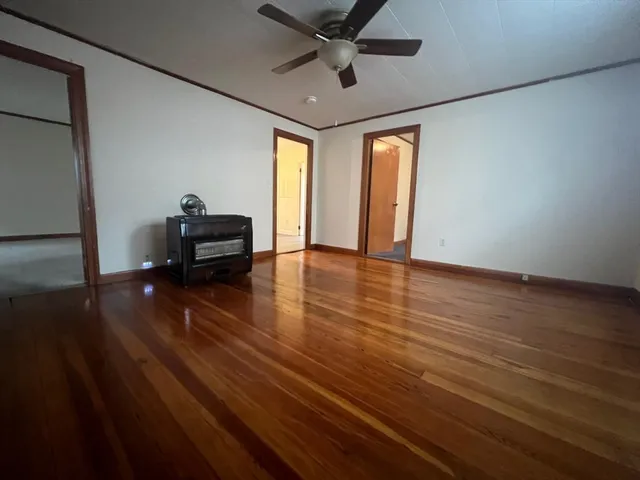 a view of an empty room with wooden floor and a ceiling fan