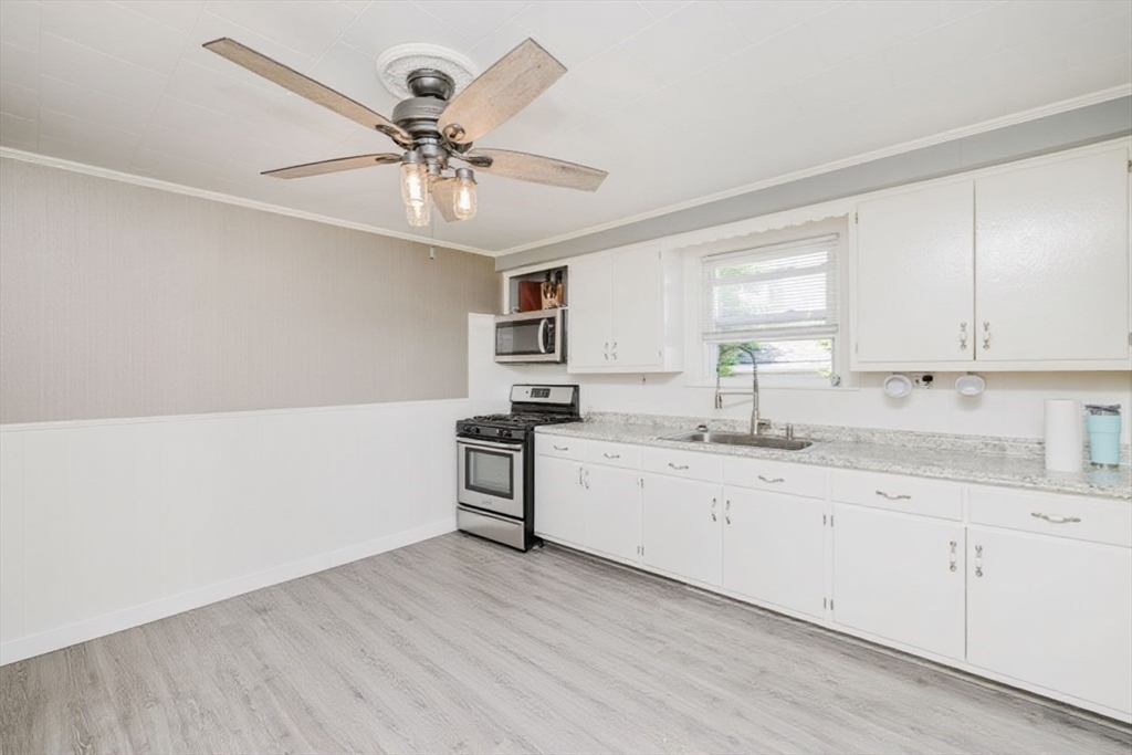 20 Wilcox Street Fall River, MA 02724 - Photo 9 of 28 a kitchen with granite countertop a stove a sink and white cabinets with wooden floor