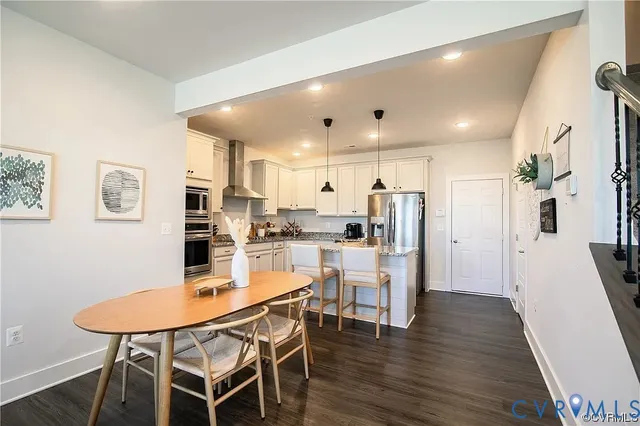 a kitchen with stainless steel appliances kitchen island granite countertop a dining table chairs and white cabinets