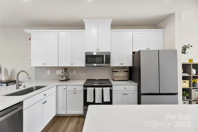 a kitchen with stainless steel appliances a refrigerator a stove top oven a sink dishwasher and white cabinets with wooden floor