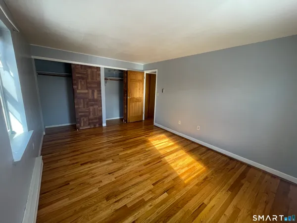 an empty room with wooden floor and windows with curtains