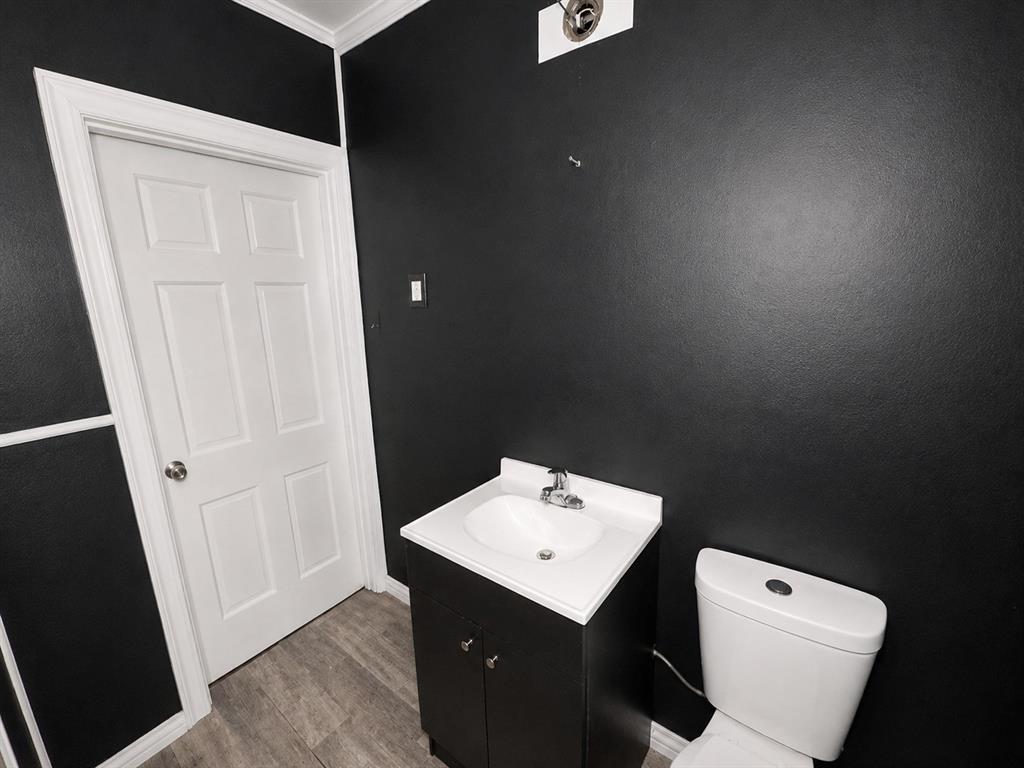 1010 Winters Street Dallas, TX 75216 - Photo 18 of 20 Black painted walls with white trim, a white paneled door, a white toilet, and a vanity with a white countertop and dark base
