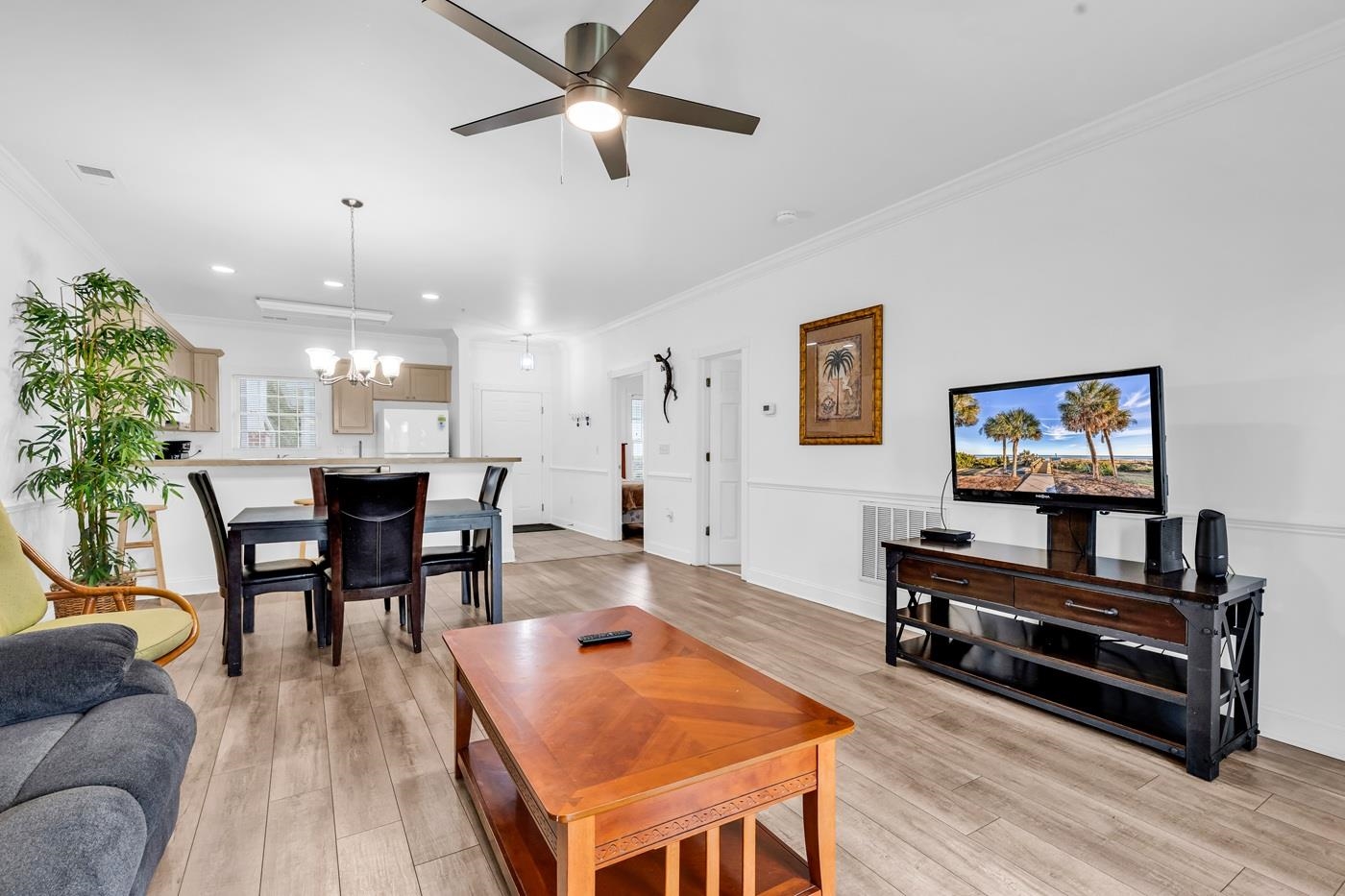 4801 Luster Leaf Circle, Unit 104 Myrtle Beach, SC 29577 - Photo 11 of 37 Living room featuring crown molding, a ceiling fan, a barn door, light wood-style flooring, and a chandelier